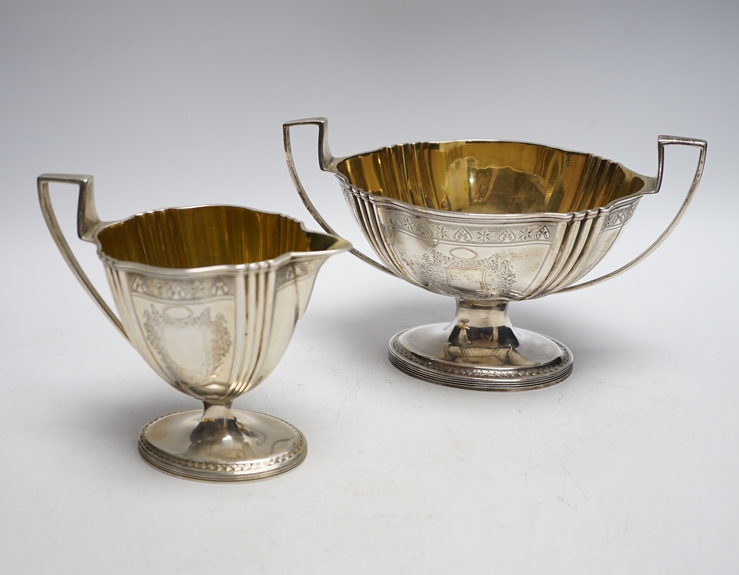 A George III engraved silver two handled oval pedestal sugar bowl and matching cream jug, Henry Chawner, London, 1792, bowl 21.2cm over handles, 20.1oz.